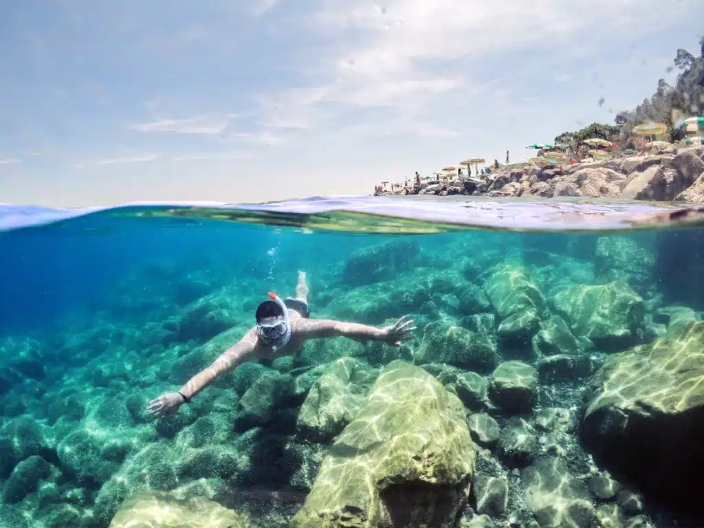 Person snorkeling on a beach with underwater rocks