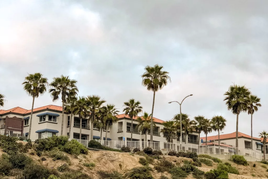 Stucco buildings sitting on a beachside cliff surrounded by palm trees