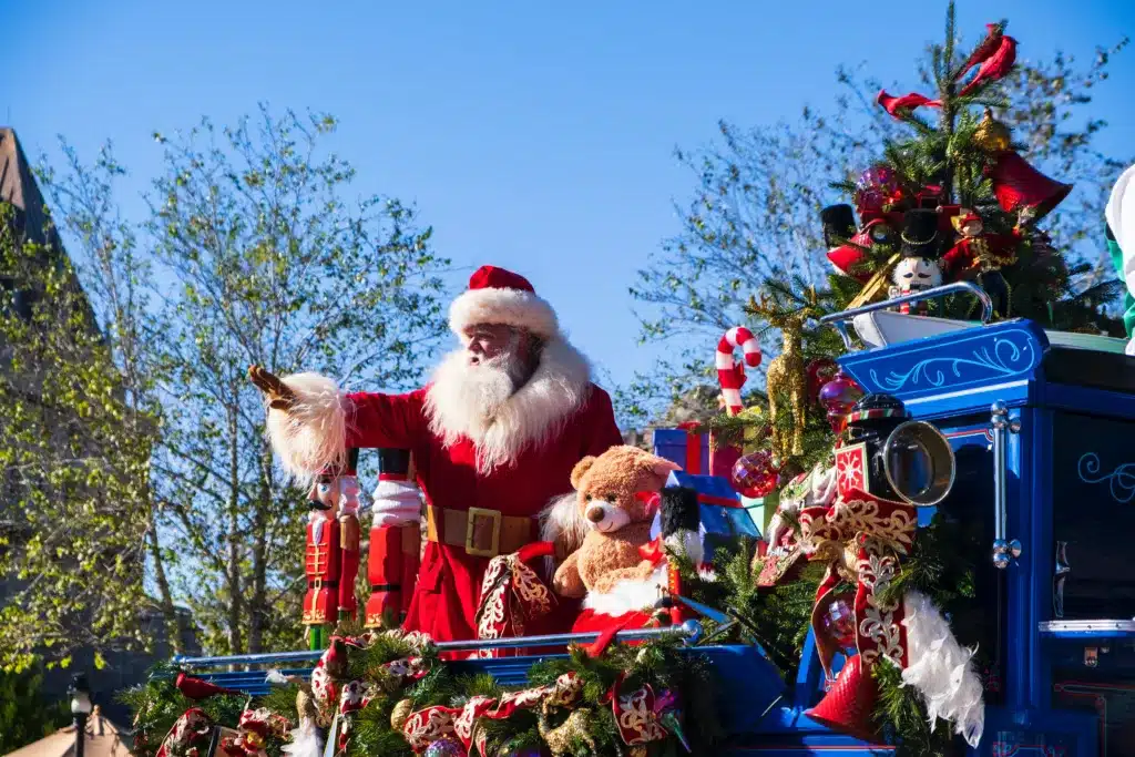 Santa Claus riding in a blue sleigh in a holiday parade