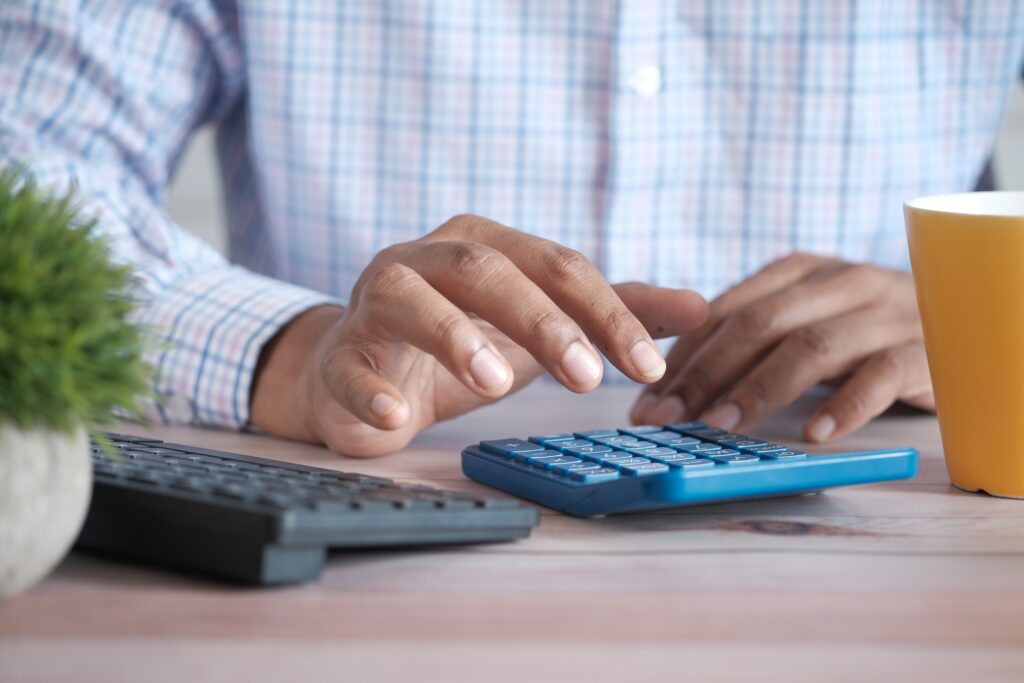 Close up of man’s hand using calculator and a black computer keyboard