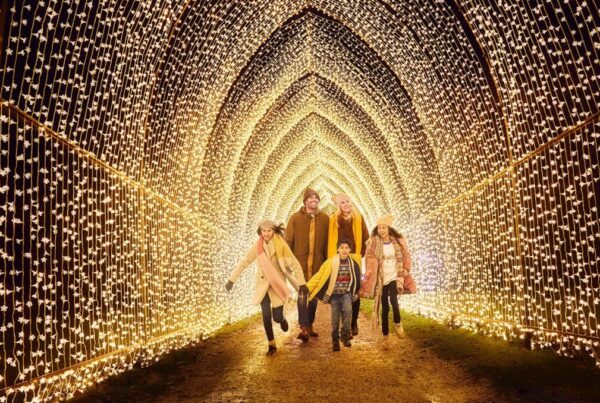Two Adults and Three Children Dressed in Winter Coats and Festive Apparel Walking Through a Tunnel of Thousands of White Christmas Lights
